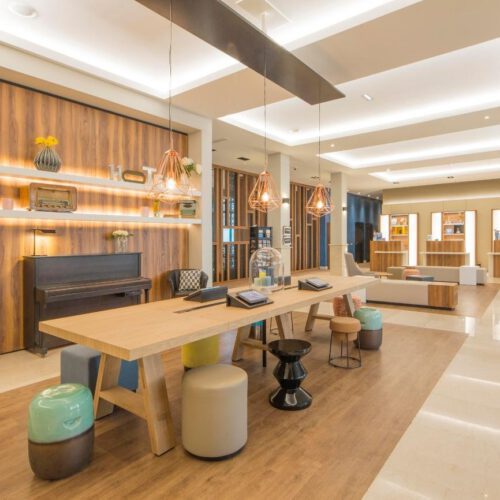 Lobby Witte kamer met houten tafels en verschillende krukjes met een zwarte piano