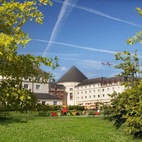 Voorkant Grand Magic hotel Wit gebouw met toren en een groot grasveld met klimrek
