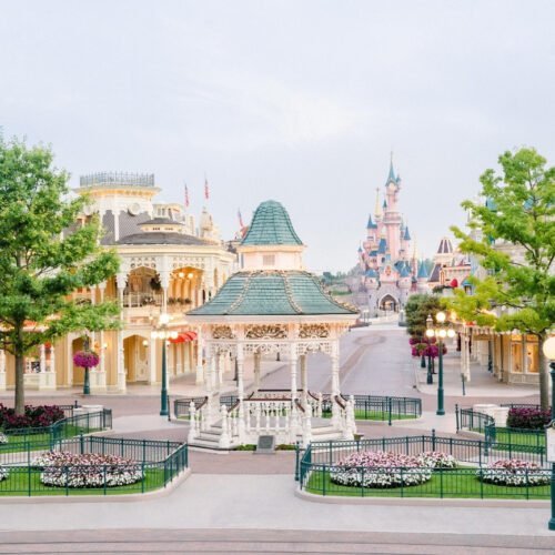 Main Street Disneyland park Victoriaanse gebouwen aan Main Street U.S.A., met twee boompjes op de voorgrond en uitzicht op het roze kasteel van Doornroosje in de verte