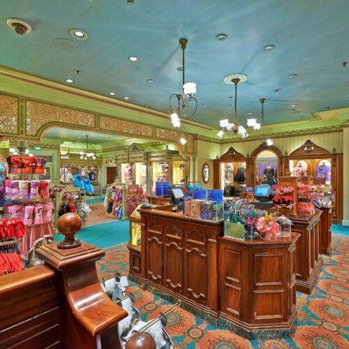 Winkel Main Street Winkel aan Main Street U.S.A.® met groene muren en een groenblauw plafond, waar diverse t-shirts, plaids en pennen worden verkocht.