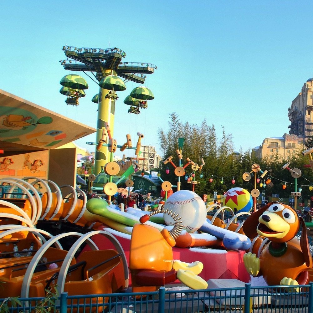 Oranje Slinky dog attractie met hondenspeeltjes en een attractie met groene parachutes op de achtergrond